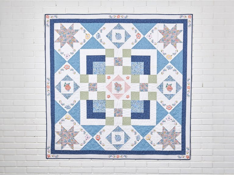 A quilt from blue, green, white and pink fabrics with printed flowers and embroidered flowers.